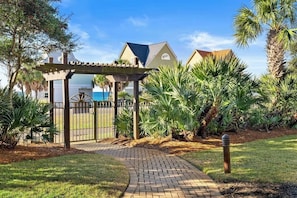 A pathway leading to a gated area with a pergola, surrounded by lush greenery and palm trees.