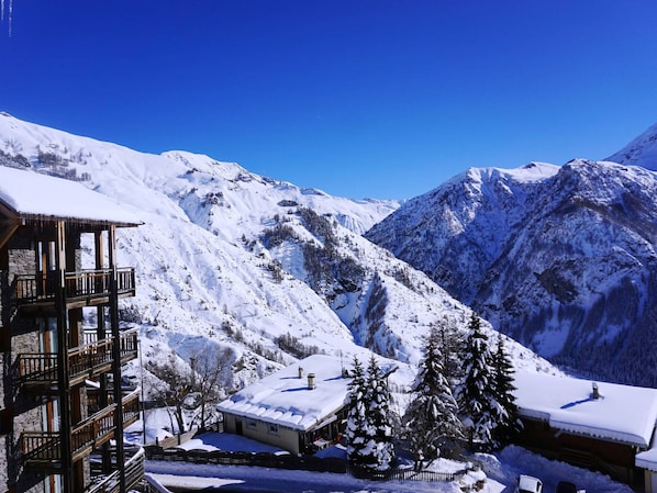 Un albergue de montaña cubierto de nieve con un balcón de madera y vistas del paisaje nevado circundante.