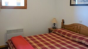 A bedroom with a bed, a nightstand with a lamp, a radiator, and a framed picture on the wall. - Bright apartment with balcony, parking, WIFI, near slopes (Orcières Merlette)