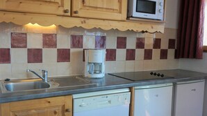 A compact kitchen with wooden cabinets, a microwave, a coffee maker, and a dishwasher. - Bright apartment with balcony, parking, WIFI, near slopes (Orcières Merlette)