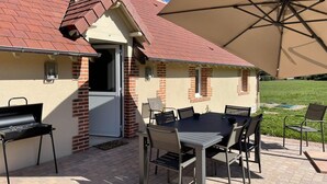Terrassa exterior amb taula i cadires, una barbacoa i un parasol gran.