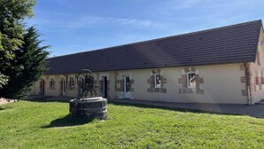 Un edifici amb teulada plana i parets de maó, una zona verda al davant i una escultura al centre.