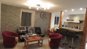 En moderne stue med sofa, stole, et sofabord og et køkkenområde med en bar.