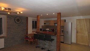 Et moderne køkken med en central ø, træbarstole, et køleskab og et ur på væggen.