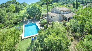 A stone house with a swimming pool surrounded by lush greenery and trees.
