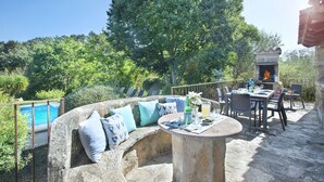 A stone outdoor seating area with a pool, surrounded by greenery and a stone fireplace.
