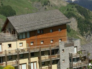 A multi-story building with wooden balconies and a stone tower, set against a mountainous backdrop.