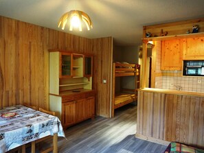 A compact kitchen with wooden cabinets, a built-in microwave, and a small dining area with a table and chairs. - Cozy studio for 4, pets allowed, near slopes, Orcières Merlette (Orcières Merlette)