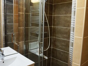 Une salle de bain moderne avec une douche à parois de verre, un lavabo blanc et des murs recouverts de carreaux de couleur brun foncé.