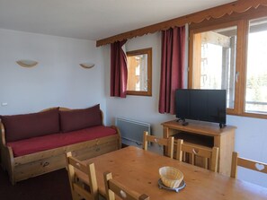 A cozy room with a wooden sofa, a dining table, and a television.
