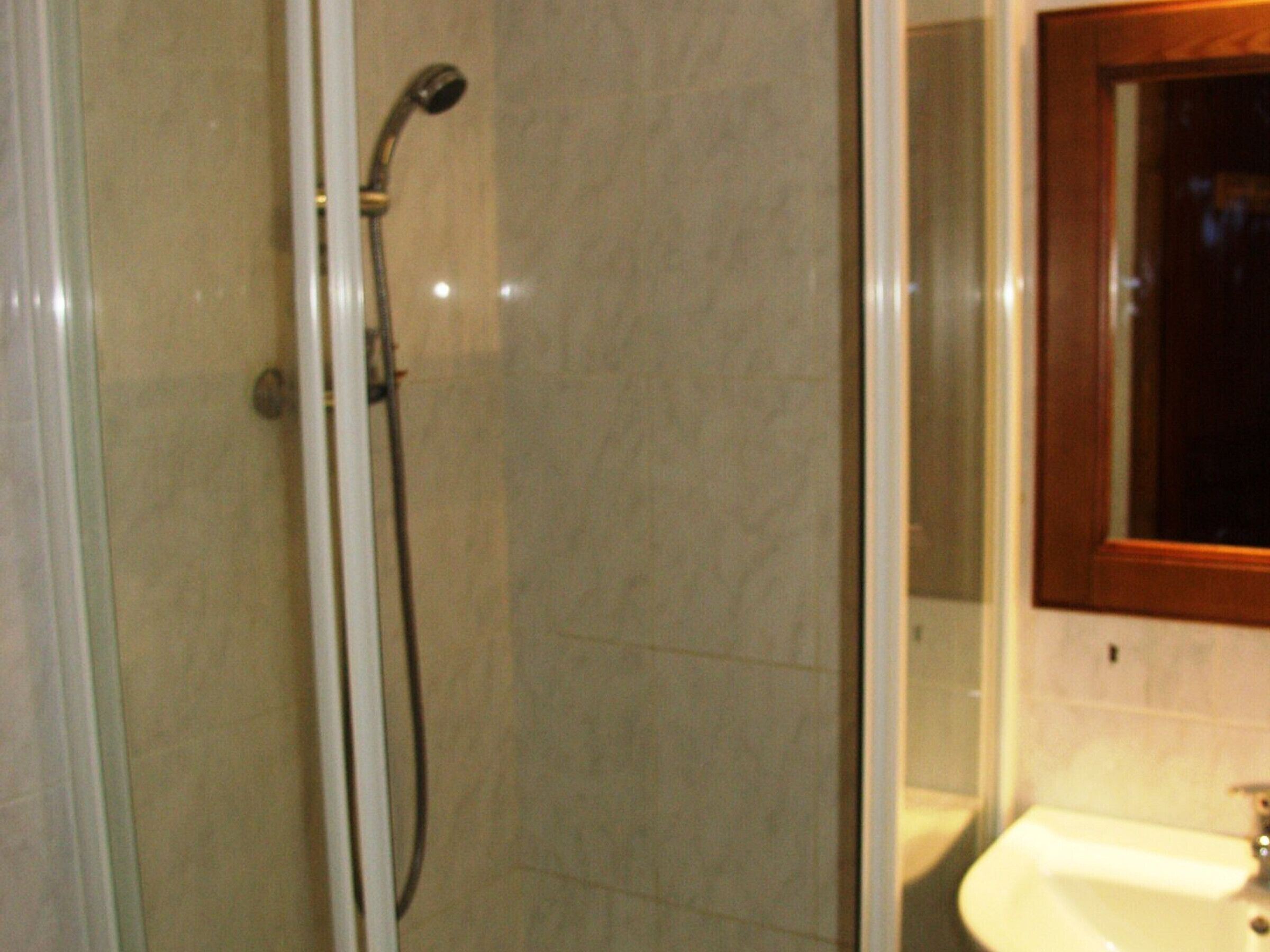 Un baño con cabina de ducha de vidrio, un lavamanos y un espejo con marco de madera.