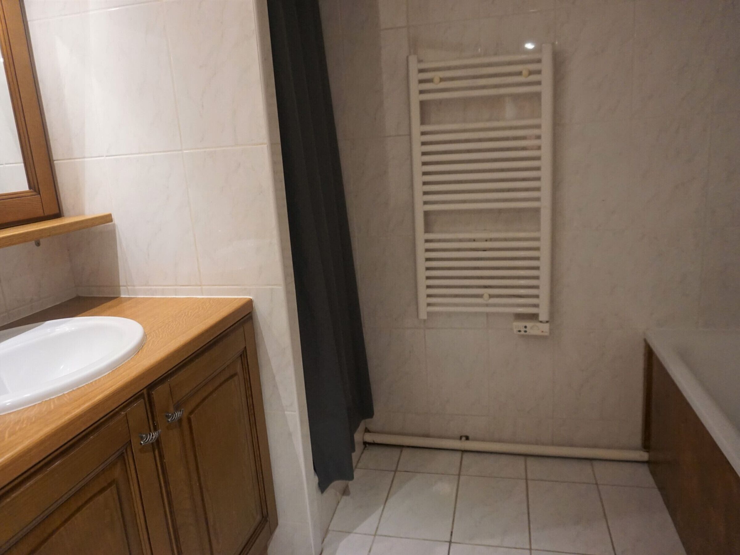 A bathroom with a white sink, wooden cabinets, a towel rack, and a shower curtain.