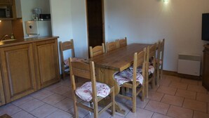 A dining area with a wooden table and chairs, a kitchen with cabinets and appliances, and a wall-mounted light fixture. - 4-room apartment, 9 pers, pets allowed, covered parking (Orcières Merlette)