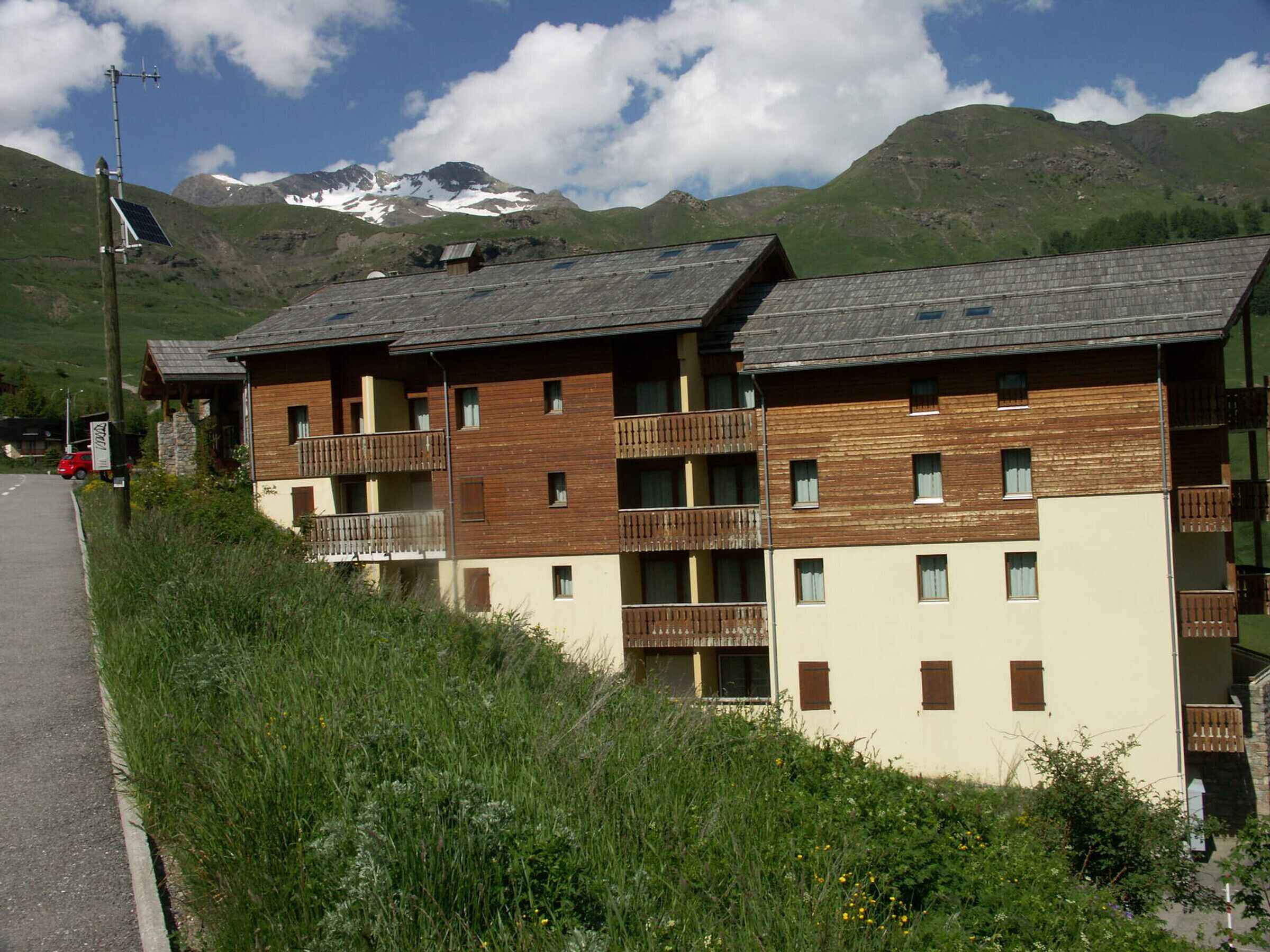 A multi-story building with balconies, a road beside it, and a mountainous backdrop.