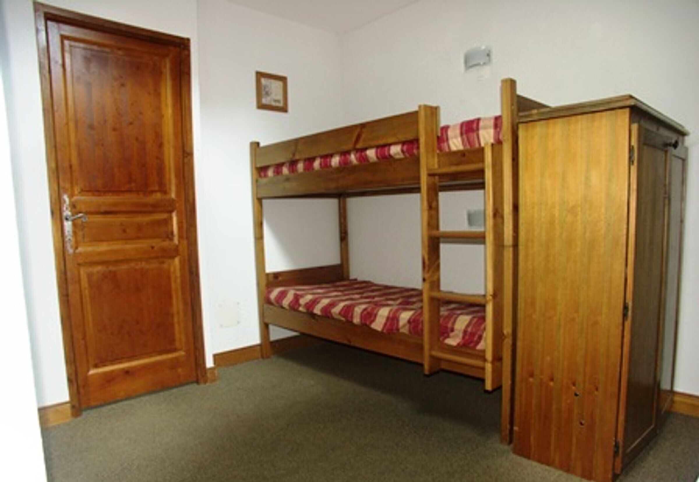 Un lit superposé avec une structure en bois et un matelas à rayures, une armoire en bois et une porte fermée.