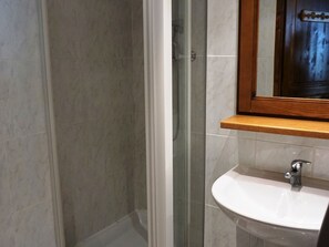 Ein Badezimmer mit Duschkabine aus Glas, einem weißen Waschbecken und einem Holzregal darüber.