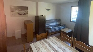 Ein kleiner, gemütlicher Raum mit einem Holztisch und Stühlen, einer Couch, einem Fernseher und einem Fenster mit Vorhängen.