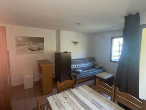 Ein kleiner, gemütlicher Raum mit einem Holztisch und Stühlen, einer Couch, einem Fernseher und einem Fenster mit Vorhängen.