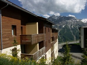 Ein mehrstöckiges Gebäude mit Holzfassade und Balkonen, vor einer gebirgigen Kulisse.