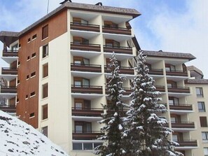 Un hôtel à plusieurs étages, doté de balcons, avec un arbre enneigé devant.