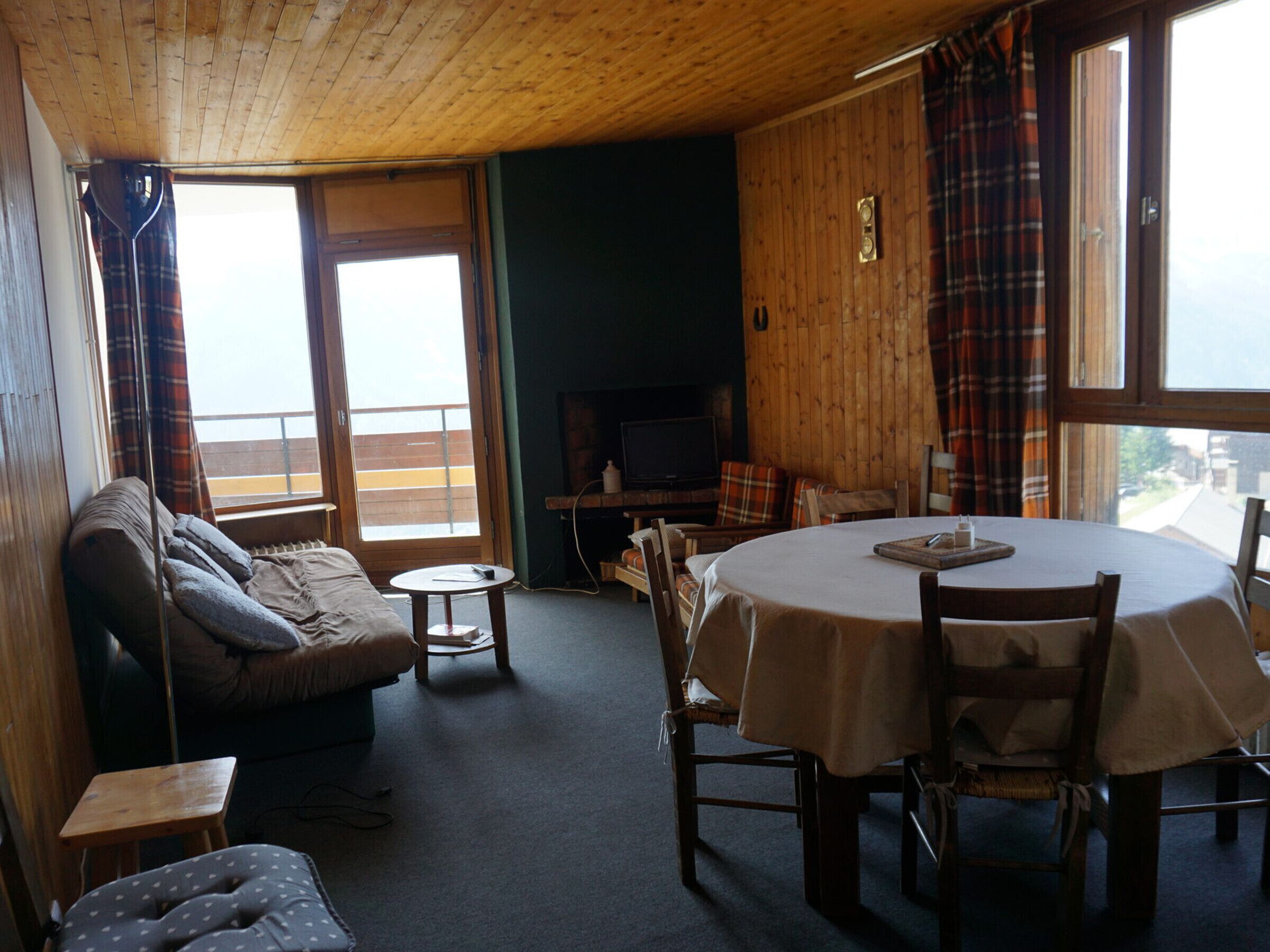 Ein gemütliches Wohnzimmer mit einer Couch, einem kleinen Tisch und einem Esstisch mit Stühlen. Ein Kamin und ein Fernseher sind ebenfalls vorhanden.