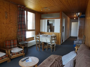 L’intérieur d’un chalet accueillant, avec un coin repas, un canapé et une petite table sur laquelle se trouve une télécommande.