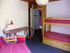 Une petite pièce, de taille modeste, comprenant un lit superposé, un bureau avec une chaise et une lampe rouge.