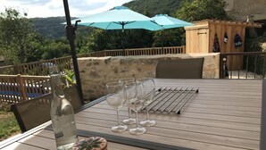 Una mesa de madera con una botella y vasos, un tendedero y un armario de madera en un entorno exterior soleado.