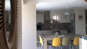 Una cocina moderna con una isla central, zona de comedor con sillas amarillas y un espejo grande a la izquierda.
