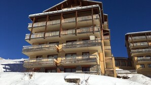 A multi-story hotel with balconies, a stone facade, and a snowy landscape. - 2-room flat, 4 pax, pool, WiFi, covered parking (Orcières Merlette)