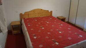 A bedroom with a wooden bed, a red bedspread, two bedside tables, a nightstand, and a wall-mounted lamp. - 2-room flat, 4 pax, pool, WiFi, covered parking (Orcières Merlette)