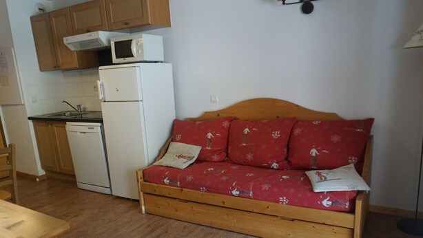 A compact kitchenette with a microwave, refrigerator, and sink. A wooden sofa with red cushions is positioned against the wall. - 2-room flat, 4 pax, pool, WiFi, covered parking (Orcières Merlette)