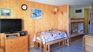 Et rum med træpaneler, et fjernsyn på et træskab, et spisebord med hvid dug, en køjeseng og et ur på væggen.