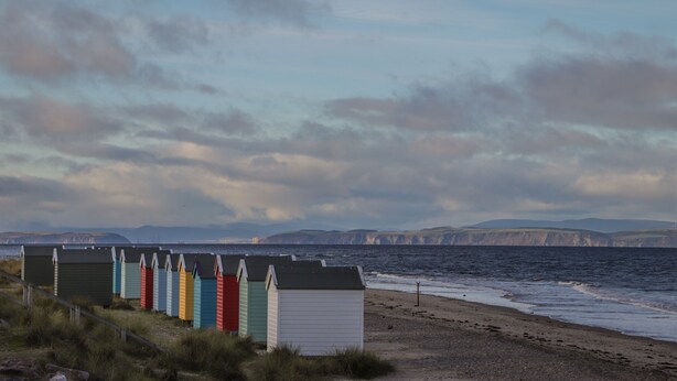A row of colorful beach huts along a coastal path with cliffs in the background. - Aurora View (Forres)