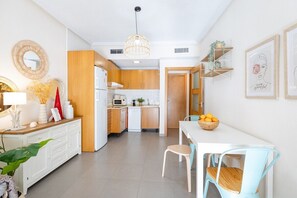 A modern kitchen with wooden cabinets, a white countertop, and a dining area with a white table and blue chairs. - Fidalsa Seaside Views (Guardamar)