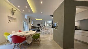 A modern dining area with a long table and colorful chairs, a kitchen in the background, and a large bull skull decoration on the wall. - LE CLOS DE PEYRUZEL (Daglan)