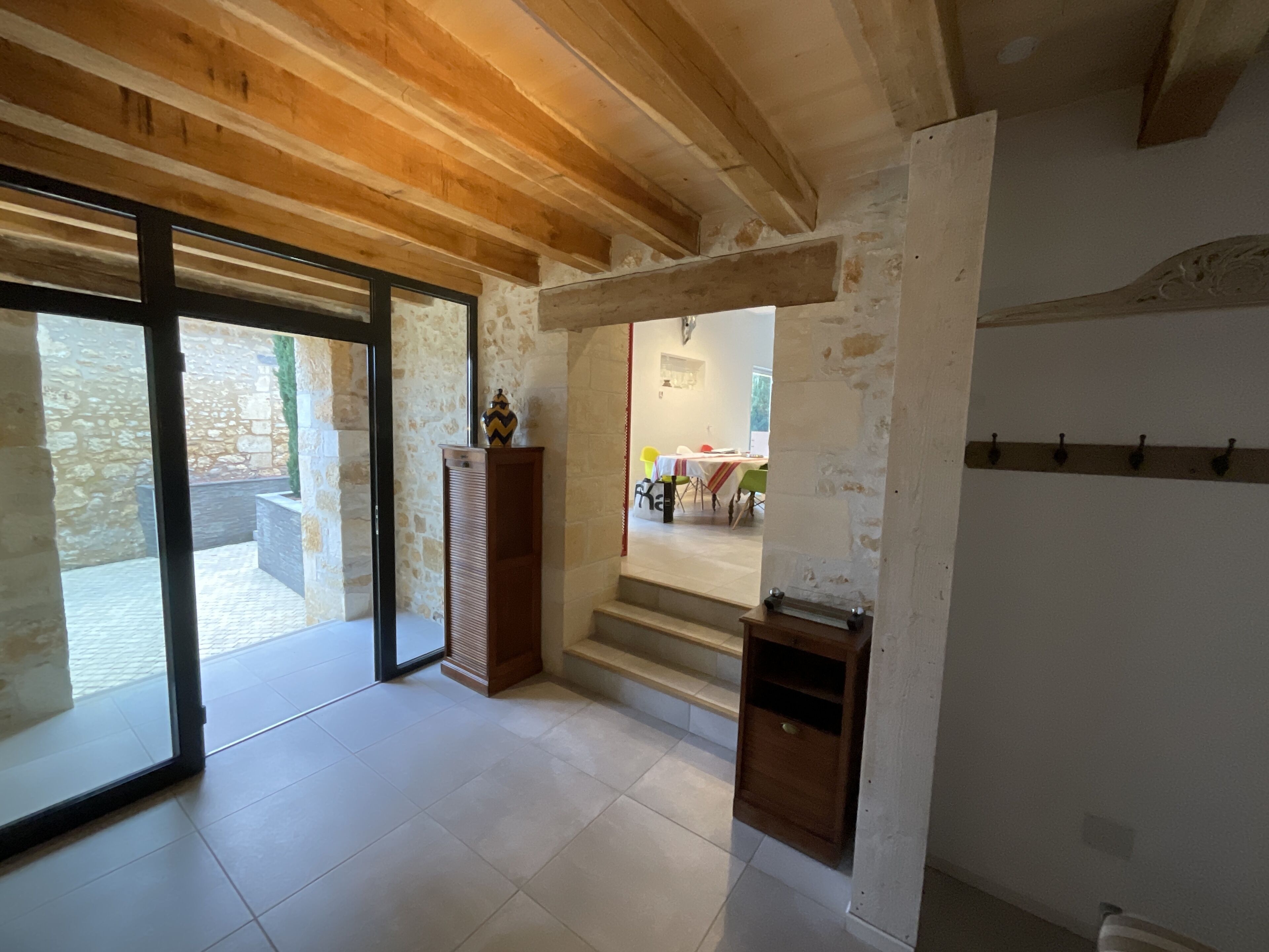 A spacious room with a wooden ceiling, a stone wall, and a view of an outdoor area with a table and chairs.