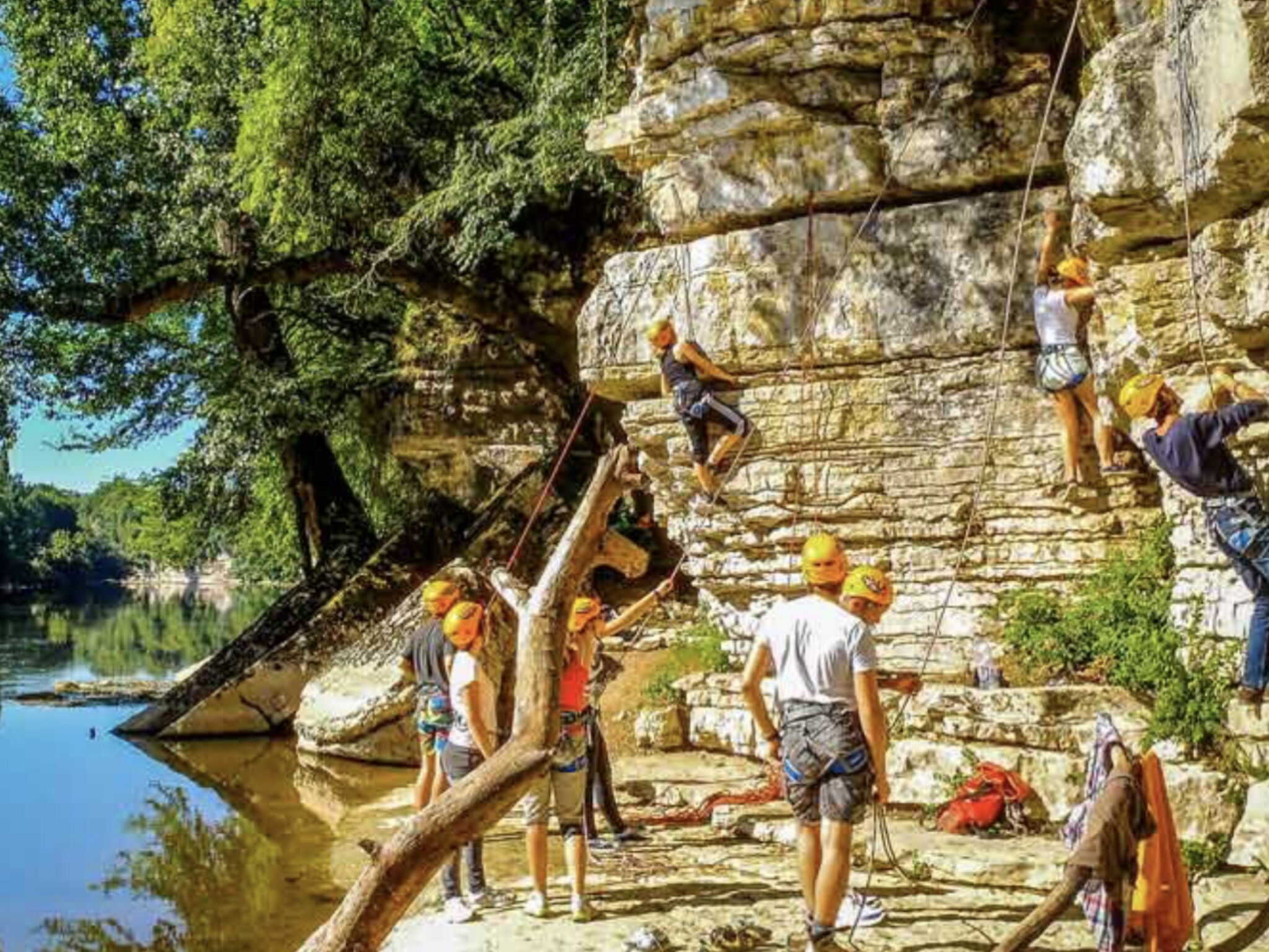 Un grup de persones escalant roques en un penya-segat al costat d'una massa d'aigua.