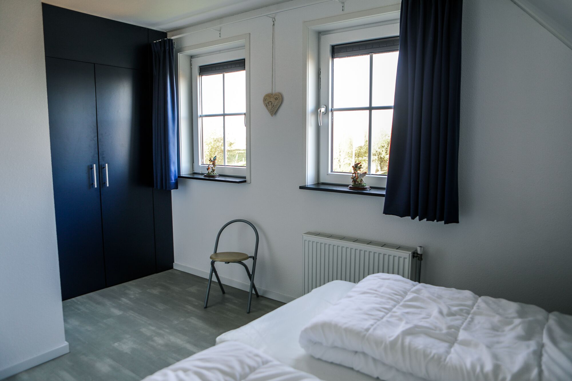 Une chambre à coucher avec un lit, un radiateur, une chaise et une armoire.