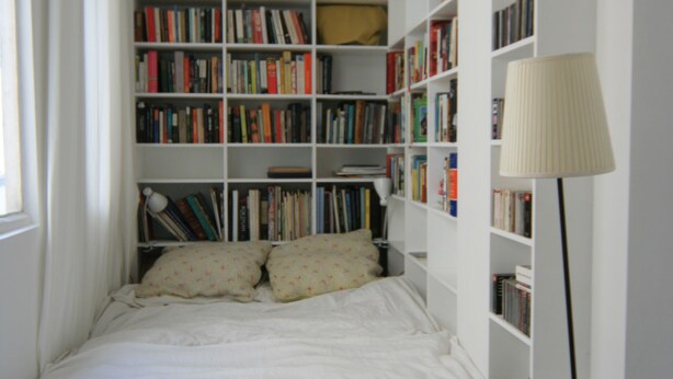 Una camera da letto con una libreria a muro, un letto con biancheria bianca e una lampada da terra.