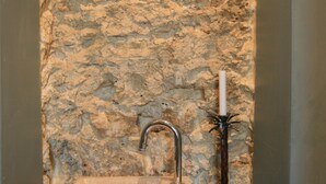 Un bagno con parete in pietra, un lavandino e un portacandele.