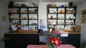 Una cucina con una tovaglia a quadri rossa e bianca, un vaso con fiori ed scaffali pieni di stoviglie e utensili da cucina.