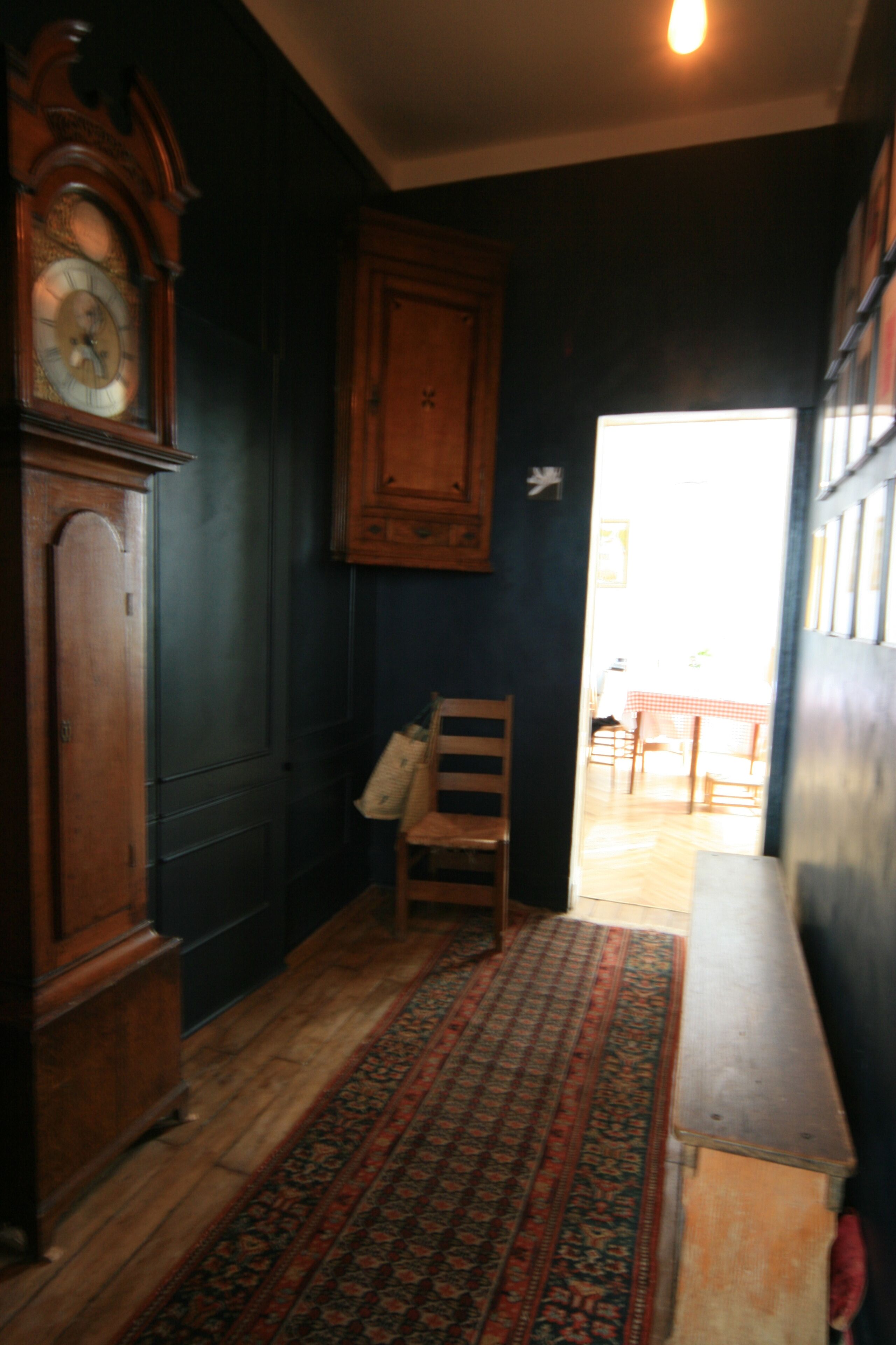 A hallway with a wooden floor, a patterned rug, a wooden chair, a wooden cabinet, and a clock.