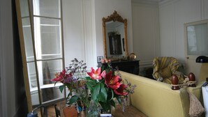 Una stanza con un'ampia finestra, uno specchio, un divano giallo e un vaso con fiori.