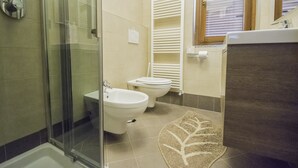Een badkamer met een douchecabine van glas, een bidet, een toilet en een handdoekrek.
