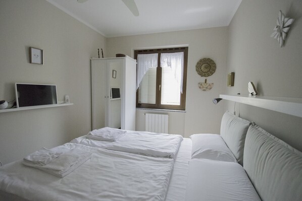 Un dormitorio con cama, televisor, armario y ventana con cortinas.