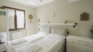 Een slaapkamer met een bed, een kaptafel, een nachtkastje, een plafondventilator en een raam met gordijnen.