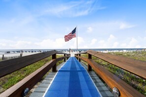 A wooden boardwalk leading to a beach with an American flag.