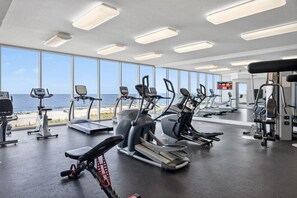 A gym with cardio machines, weight training equipment, and large windows overlooking the sea.
