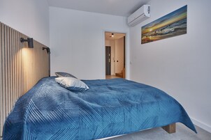 Un dormitorio con una cama, una lámpara de pared, un cuadro y un aire acondicionado.